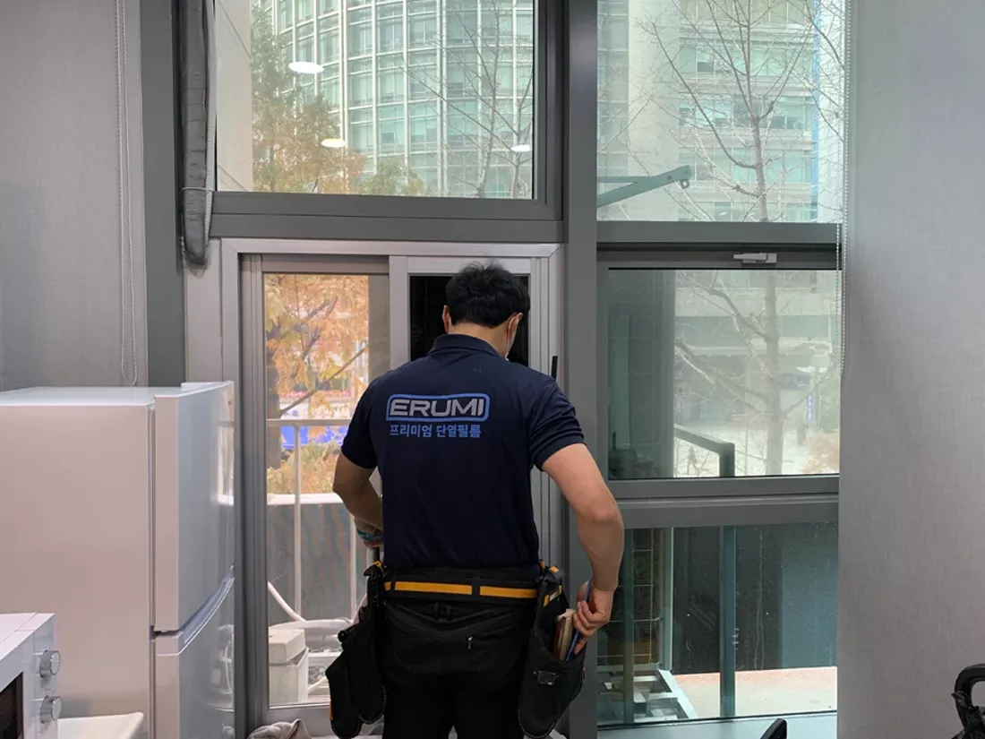 기술자가 창틀에서 열차단 필름을 부착하는 시공 모습
