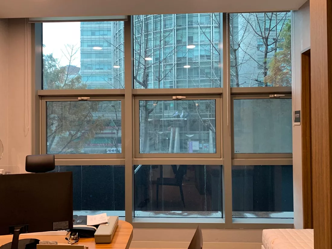 책상 옆 통유리창으로 보이는 맞은편 건물과 가로수