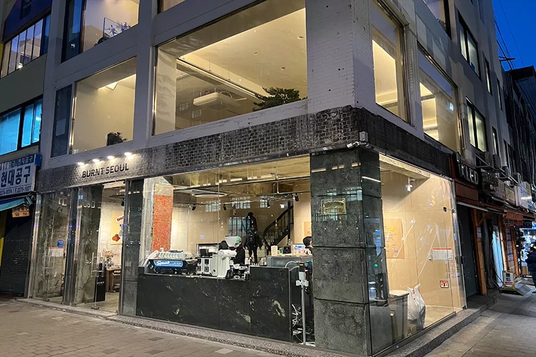 저녁 시간 통유리 너머로 따뜻한 조명이 비치는 카페 외관 전경